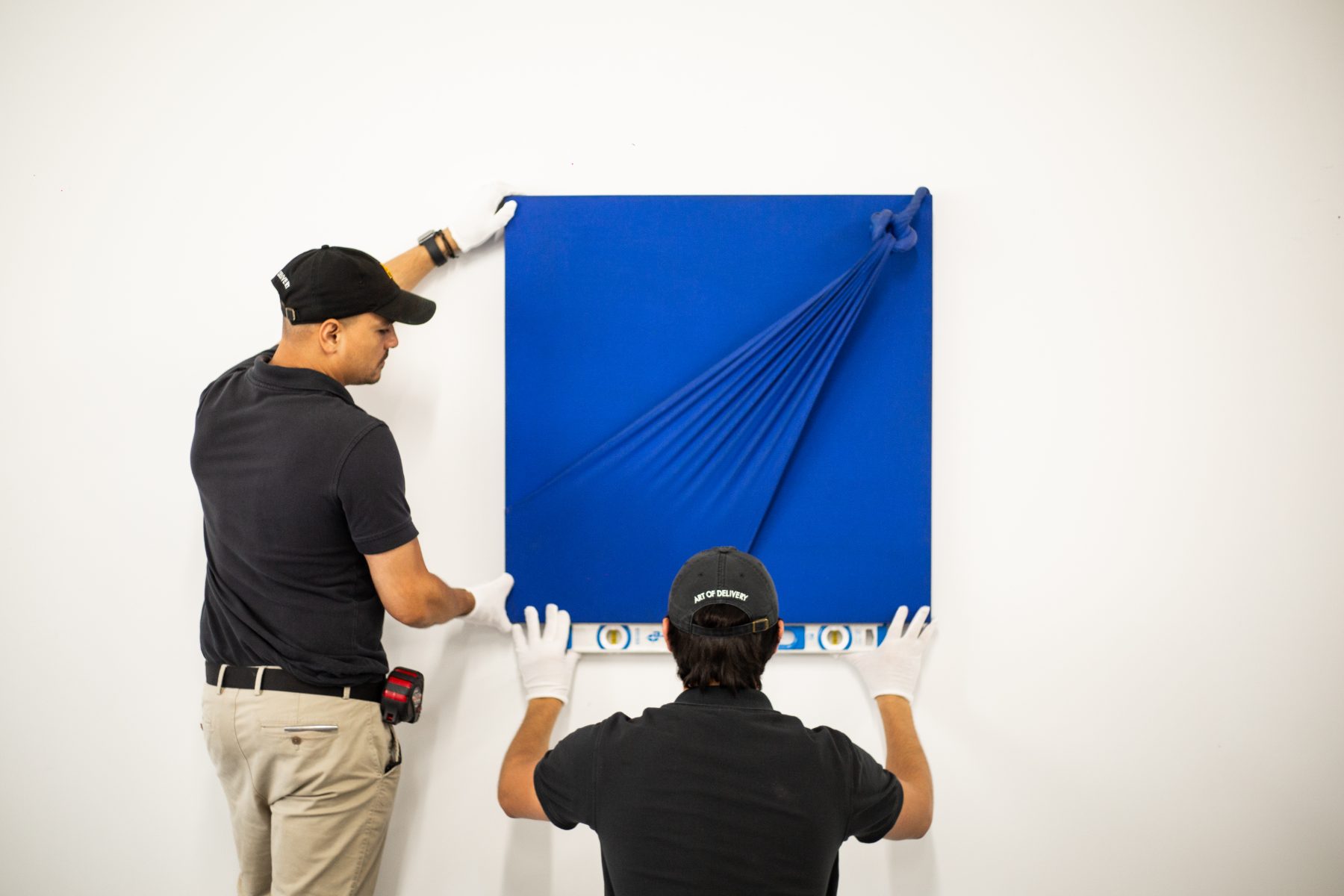 White-gloved crew leveling a blue monochrome canvas on a gallery wall