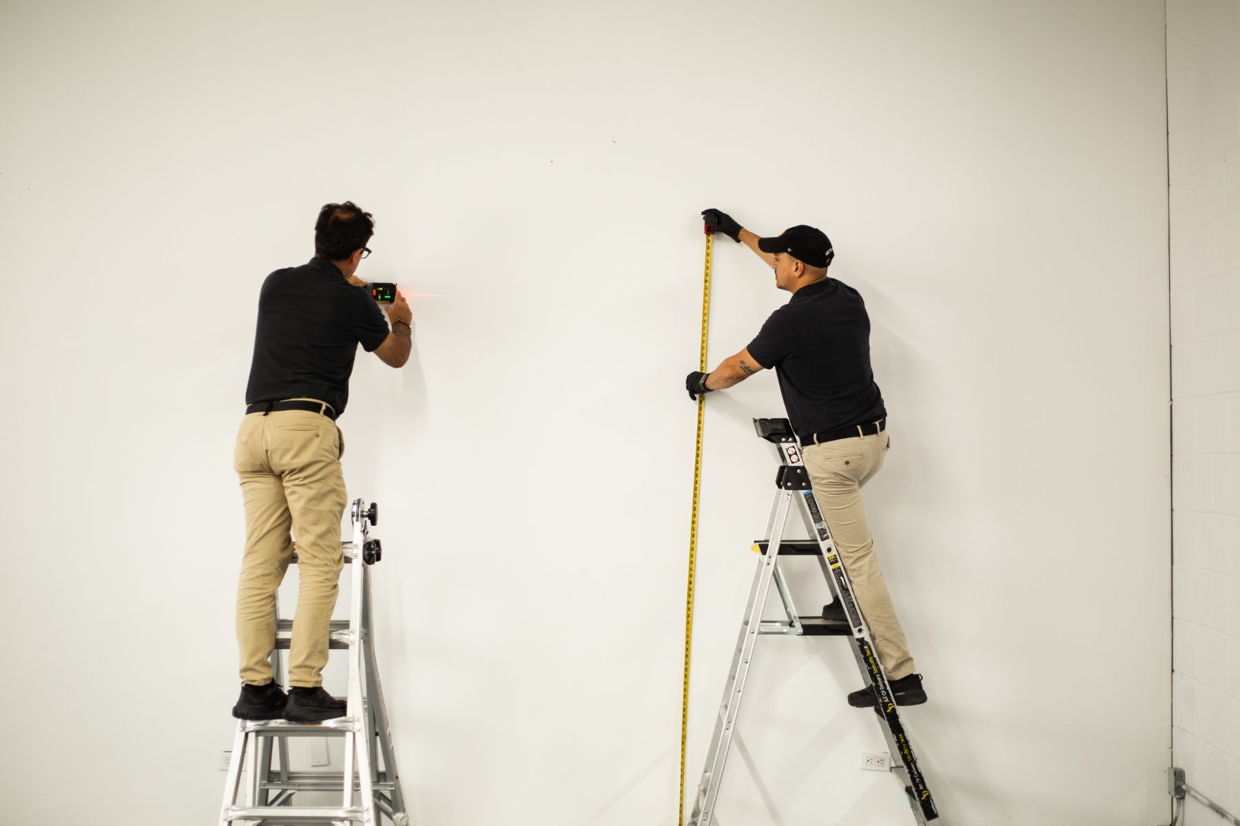 Two specialists measuring and laser-leveling a wall before an install