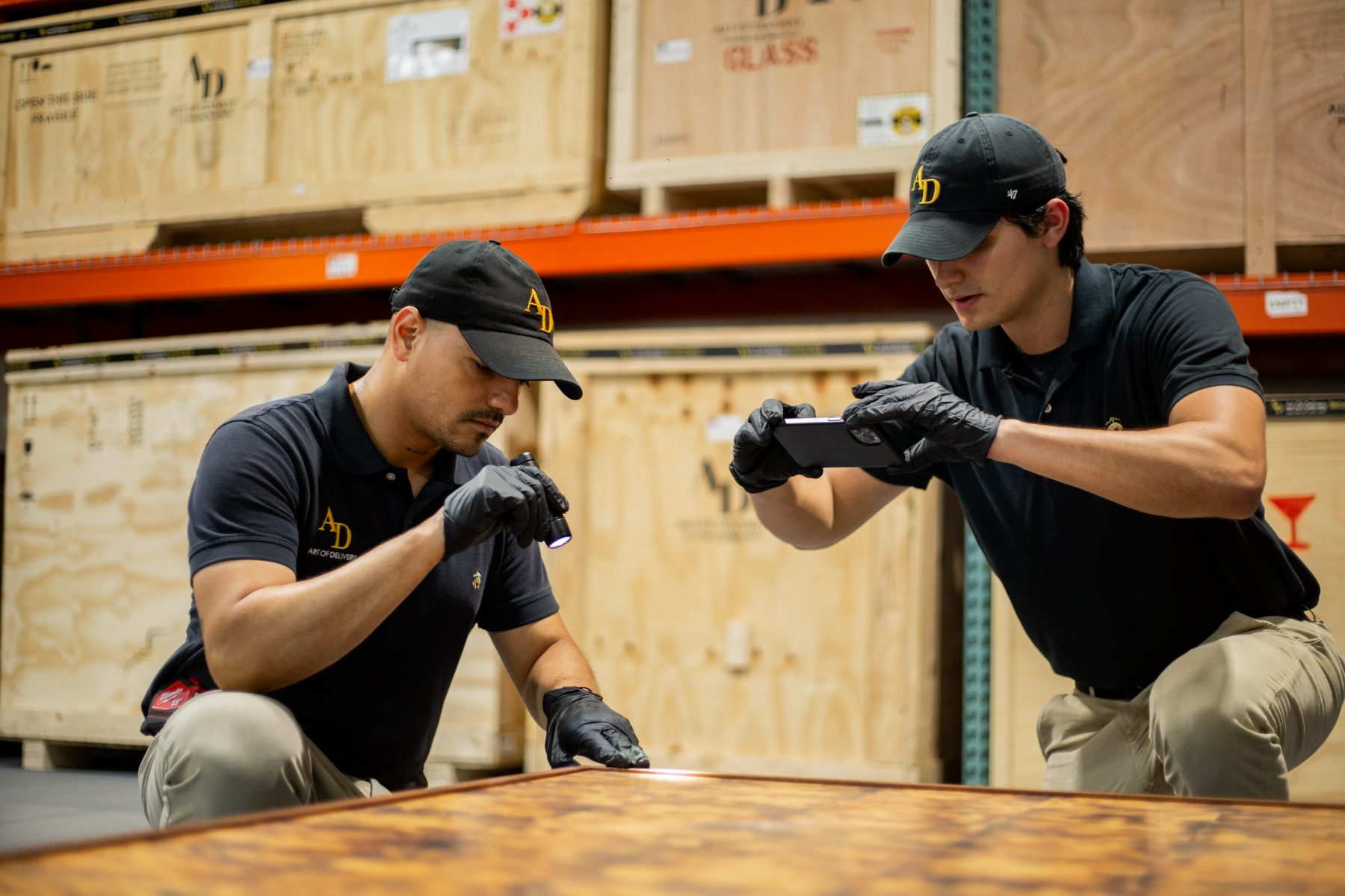 Two Art of Delivery specialists condition-checking and photographing a table top in the warehouse